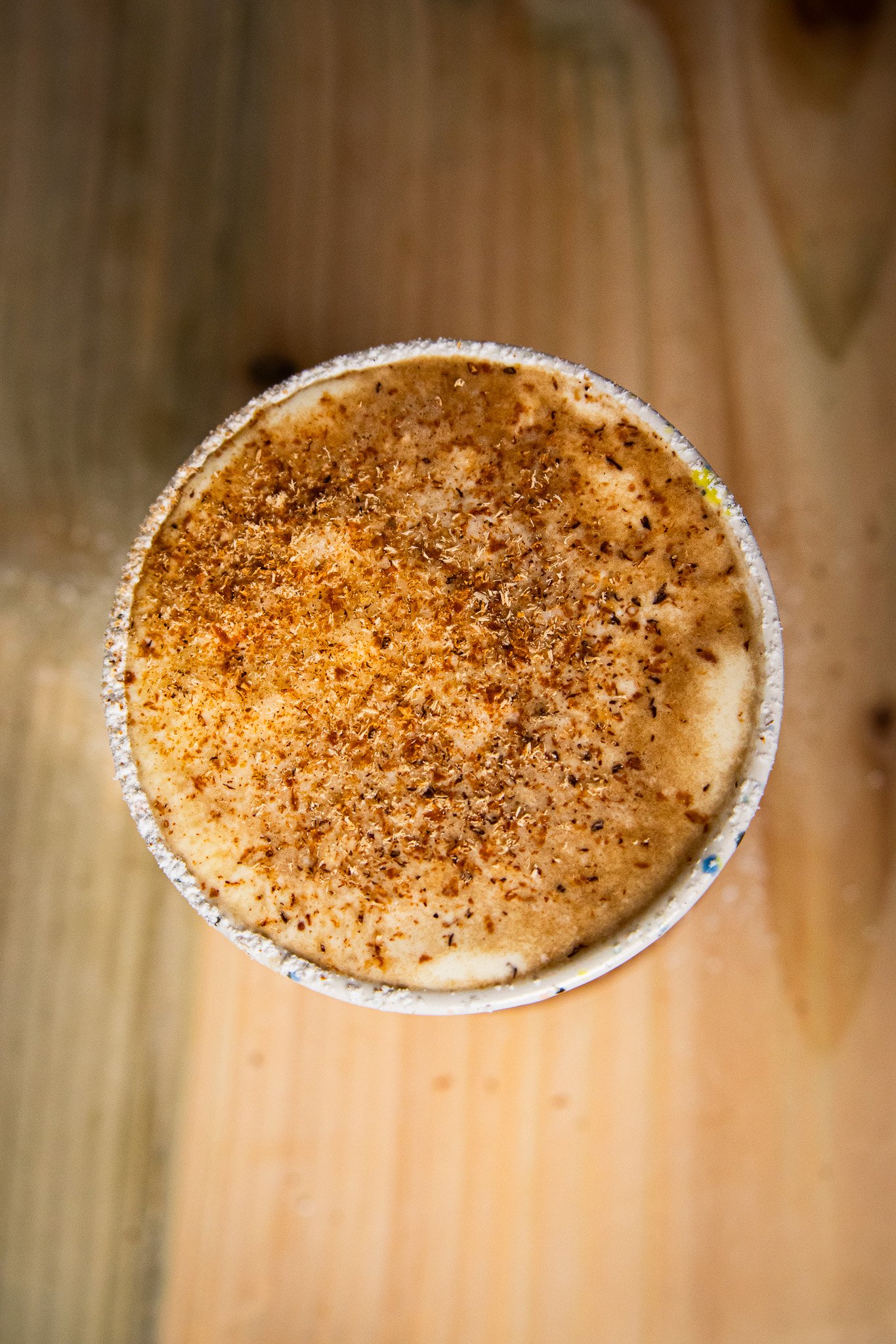 Overhead view of a spiced Irish coffee topped with grated nutmeg and foam in a speckled ceramic tumbler